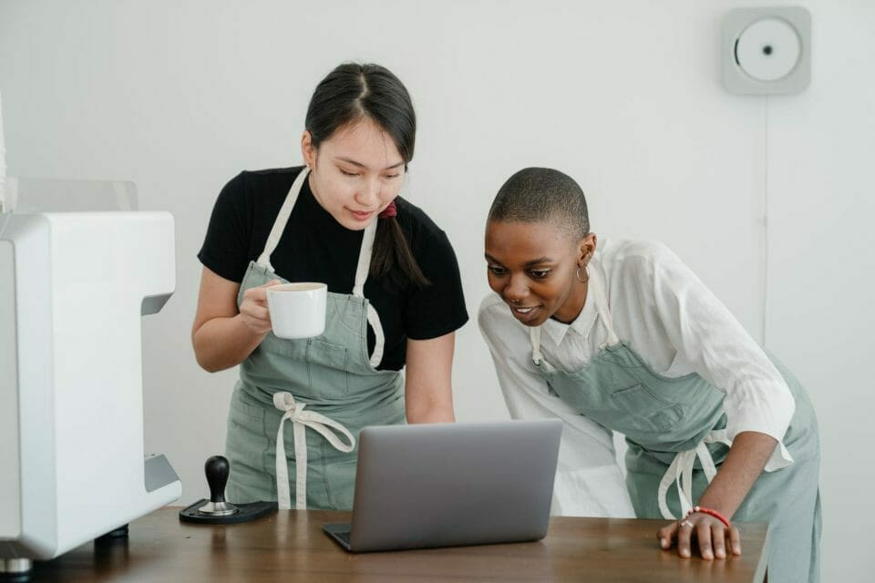 diverse female baristas communicating while using laptop at work
